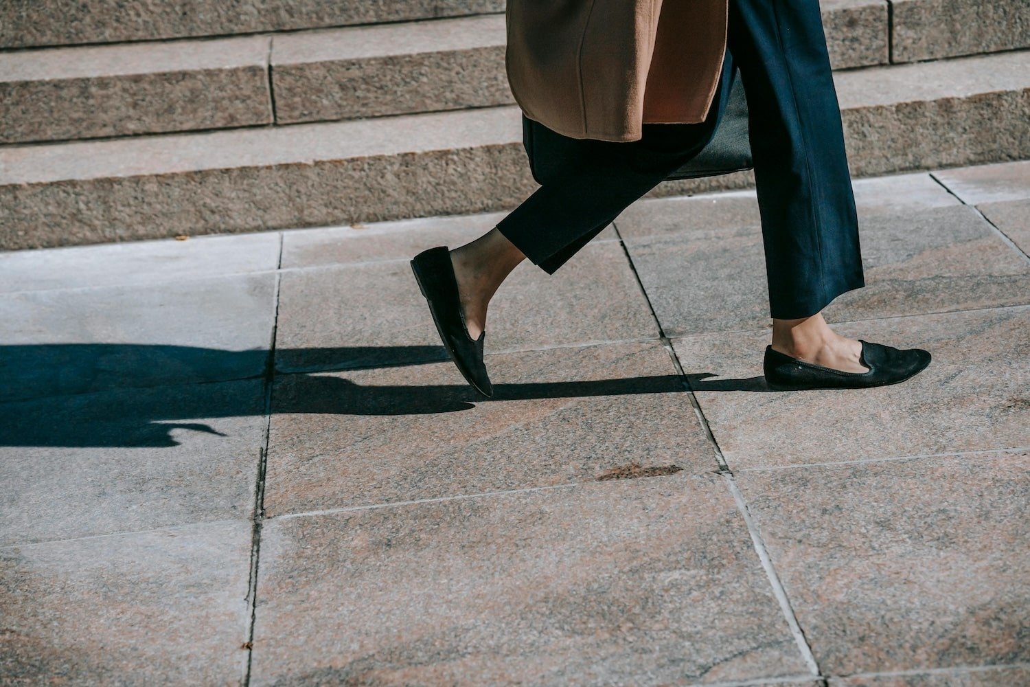 image of woman's legs from knee down carrying brown handbag, cropped blue pant and wearing loafers